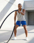 Man exercising in flow shorts, using battle ropes in a modern gym setting with natural light.