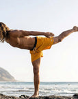 Man practicing yoga in Flow shorts - Saffron by the beach, showcasing flexibility and movement.
