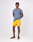 Man wearing Flow shorts in saffron color with a blue t-shirt and sandals, showcasing a stylish and comfortable look.