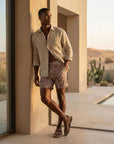 Man wearing 4-way stretch Swerve Shorts in Smoky Quartz, standing by a pool in a desert setting.