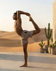 Man practicing yoga in 4-way stretch Swerve Shorts - Smoky Quartz against a desert backdrop.