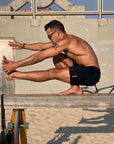 Man performing a stretch on a balance beam wearing 4-way stretch swerve shorts in Crow Black.