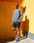 Model wearing 4-way stretch swerve shorts in Crow Black and a gray sweatshirt, standing against a colorful wall.