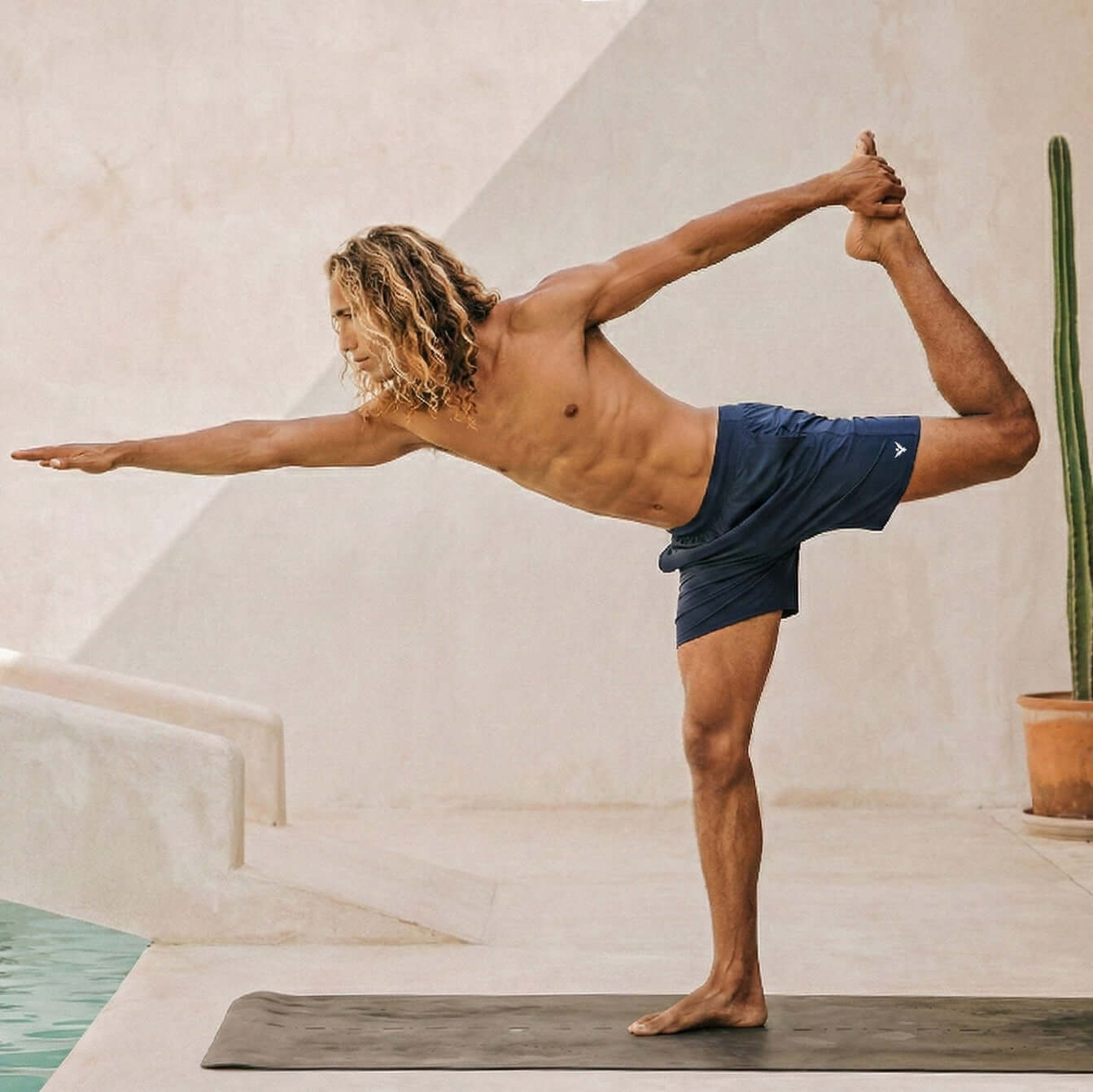 Man practicing yoga in 4-way stretch Swerve Shorts in Midnight Blue by the poolside.