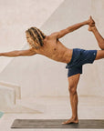 Man practicing yoga in 4-way stretch Swerve Shorts in Midnight Blue by the poolside.